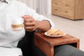 Cookies on sofa armrest wooden table. Man holding cup of coffee at home, closeup