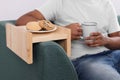 Cookies on sofa armrest wooden table. Man holding cup of drink at home, closeup Royalty Free Stock Photo