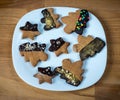 Cookies on a white plate, wooden brown background. Christmas tree or stars shaped cookies.