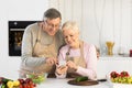 Happy Senior Couple Using Smartphone Preparing Dinner Standing In Kitchen Royalty Free Stock Photo