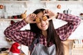 Happy woman in apron holding star shaped cookies in front of her eyes on home kitchen background