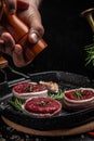Cooking Beef medallions wrapped in bacon with rosemary and spices on grill pan by chef hands on black background Royalty Free Stock Photo