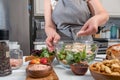 Cooking Caesar salad. Cook adds grated parmesan to glass bowl with salad in a home kitchen