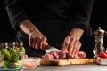 Cooking, the chef cuts pork meat on a background of vegetables. Cooking. Recipe book, cooking and gastronomy Royalty Free Stock Photo