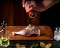 Cooking a chicken leg with the hands of a chef on a dark background. Add pepper to chicken meat. Free advertising space for a Royalty Free Stock Photo