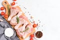 Cooking chicken legs with seasonings and tomatoes on wooden cutting board over white table background Royalty Free Stock Photo