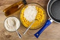 Cooking corn pancakes. Bottle of vegetable oil, bowl with flour, fork in bowl with mix of eggs, flour and corn, frying pan on Royalty Free Stock Photo