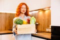 Cooking, culinary and people concept - happy smiling woman in apron with food in wooden box over kitchen background Royalty Free Stock Photo