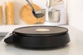 Cooking delicious crepe on electric pancake maker in kitchen, closeup Royalty Free Stock Photo