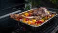 Cooking a delicious leg of lamb on a BBQ with peppers and potatoes in metal tray Royalty Free Stock Photo