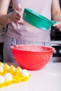 Cooking Easter cake at home in the kitchen. Sifting flour through a green sieve in female hands into a red bowl next to the