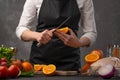 Cooking festive chicken for baking, the chef cuts an orange against a background of vegetables and fruits. Recipe book and