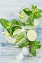 Cooking fresh cold summer beverage mojito with lime, leaf mint, straw, ice cubes, soda on white wood background.