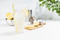 Cooking fresh summer homemade lemonade in misted glass with ingredient, yellow lemons, cutting board, shaker in soft light white. Royalty Free Stock Photo