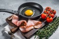 Cooking fried Egg in a skillet with bacon and tomato. Gray background. Top view Royalty Free Stock Photo