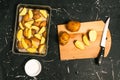 Cooking fried potatoes. Peeled and chopped potatoes laid in a baking sheet. Wooden cutting board, knife and salt against a dark Royalty Free Stock Photo