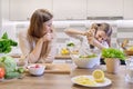 Cooking healthy home meal by family. Girl salts freshly cooked salad, mother looks up and rejoices