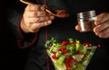 Cooking a healthy salad with the hands of a chef using fresh vegetables for lunch. Adding spices to a bowl of vegetables. Royalty Free Stock Photo