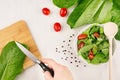 Cooking healthy vegetarian spring salad - fresh greens, tomatoes, pepper and hand with knife on white wood background, top view. Royalty Free Stock Photo