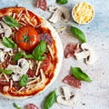 Cooking Italian pizza with tomato sauce, fresh tomatoes, cheese, mushrooms, salami slices and basil . Royalty Free Stock Photo