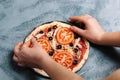 Cooking Italian pizza with tomatoes, chicken, olives on wooden background. Tomato sauce on the dough by woman`s hand