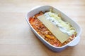 Cooking lasagna, layers of Bolognese sauce, flat pasta sheets, cream or bechamel and cheese in a casserole dish on a wooden