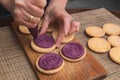 Cooking macarons cookies at home. Female hand squeezes cream on homemade cookie .on a wooden board Royalty Free Stock Photo