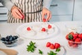 Cooking, making homemade meringue. Female hands decorating pavlova cakes with fresh berries on the kitchen table with Royalty Free Stock Photo