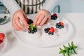 Cooking, making homemade meringue. Female hands decorating pavlova cakes with fresh berries on the kitchen table with Royalty Free Stock Photo