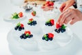 Cooking, making homemade meringue. Female hands decorating pavlova cakes with fresh berries on the kitchen table with Royalty Free Stock Photo