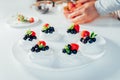 Cooking, making homemade meringue. Female hands decorating pavlova cakes with fresh berries on the kitchen table with Royalty Free Stock Photo