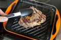 Cooking meat on cast iron grill pan indoors at home. Person turning ribeye steak on other side with tongs Royalty Free Stock Photo