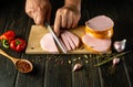 Cooking a meat dish. Slicing sausage by the hands of a cook on a cutting board. Work environment on kitchen table with spices and Royalty Free Stock Photo