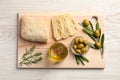 Cooking oil in jug, olives, rosemary and ciabatta bread on wooden table, flat lay