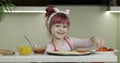 Cooking pizza. Little child in apron adding sliced tomatoes to dough in kitchen