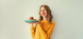 Cooking, portrait of happy smiling young woman housewife holding plate with stack of pancakes with strawberries on gray wall