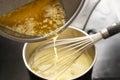Cooking process of hollandaise sauce, pouring melted butter into the pot with egg mixture, whisking all the time at low