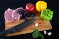 Cooking process. Meat stakes lie near knife on black background. Red tomato, green, yellow pepper, garlic, basil, pepper Royalty Free Stock Photo