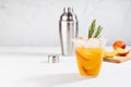 Cooking of refreshing juicy peach cocktail with ice, rosemary, sugar rim in misted glass, ingredients, silver shaker on white wood