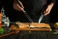 Cooking salmon fish steak by cook hands on the kitchen table in the saloon. Fork and knife for slicing fish in the hands of a chef Royalty Free Stock Photo