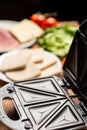 Cooking sandwiches in a sandwich maker. Different ingredients - bread, cheese, vegetables on a wooden background Royalty Free Stock Photo