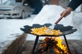 Cooking and stirring potatoes in a flat pan on the bonfire outdoor of winter