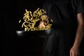 Cooking Thai food with noodles in the restaurant. The cook throws food into a hot pan. Place for advertising on a black background Royalty Free Stock Photo