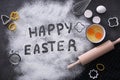 Cooking tools, ingredients for cake and words Happy Easter written in flour on black table, flat lay