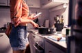 Cooking and using mobile phone. Woman preparing food and holding a smartphone to read recipe online. Student preparing dinner.