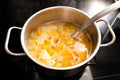 Cooking a vegetarian pumpkin soup from Hokkaido or red kuri squash in a steel pot on a black stove, vegetable autumn meal, Royalty Free Stock Photo