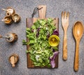 Cooking vegetarian salad with herbs, butter, salt, pepper mill, a wooden spoon and fork the salad on wooden rustic background Royalty Free Stock Photo