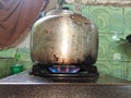 cooking water in a kettle on a gas stove, the flames are blue and red, the wall behind it is covered with green ceramics Royalty Free Stock Photo