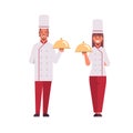 Cooks couple professional chefs holding covered platters serving trays woman man restaurant workers in uniform standing