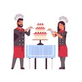 Cooks couple professional pastry chefs decorating tasty wedding cream cake woman man restaurant workers in uniform